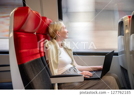 Woman working on laptop while traveling by train in daylight, concept of remote work and travel 127762185