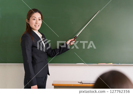 A female teacher standing at the podium with a pointer 127762356