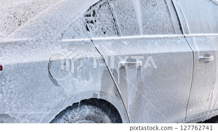 Water is sprayed on a silver sedan during a car wash activity outside. High quality photo 127762741