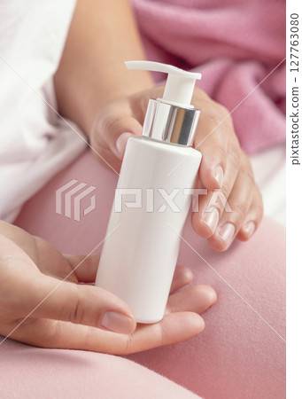 Closeup of female in pink pyjamas holding white cosmetic one pump bottle in hands, lotion mockup Closeup of female in pink pyjamas holding white cosmetic one pump bottle in hands, lotion mockup 127763080