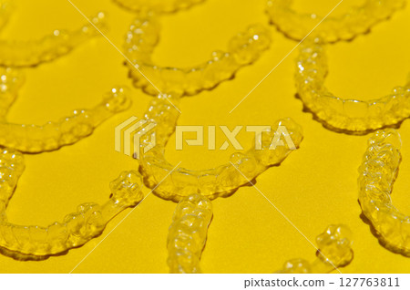 Clear dental aligners on colored yellow background, close-up side view from above. Pattern of clear braces 127763811