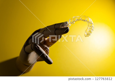 Wooden hand of an impersonal mannequin holds transparent polymer dental aligners on a colored background for teeth alignment. Aesthetic and comfortable teeth alignment 127763812
