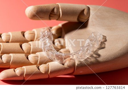 Wooden beautiful hand holds one transparent dental aligner in palms. concept of even healthy teeth Wooden beautiful hand holds one transparent dental aligner in palms. concept of even healthy teeth 127763814