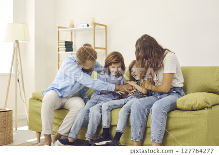 Young carefree couple is playing and having fun with their little twin sons at home. 127764277