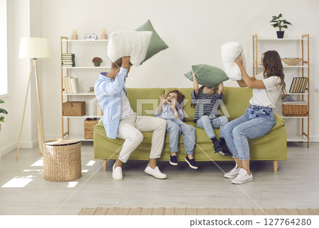 Happy young mother, father and children having a pillow fight on sofa in living room Happy young mother, father and children having a pillow fight on sofa in living room 127764280