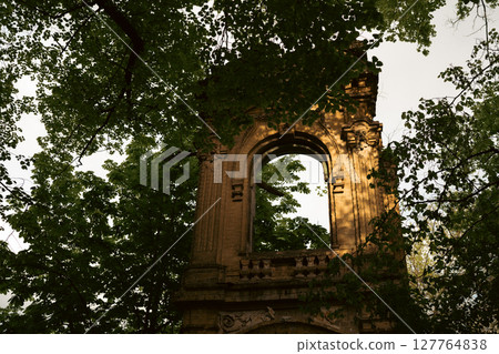 Surrounded by vibrant green leaves, the stone archway exudes a timeless elegance and tranquility. Surrounded by vibrant green leaves, the stone archway exudes a timeless elegance and tranquility. 127764838