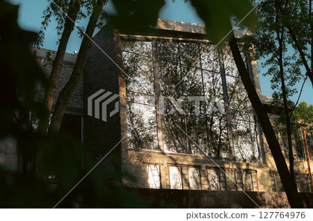 A modern building with large glass windows reflects the surrounding trees and sky A modern building with large glass windows reflects the surrounding trees and sky 127764976