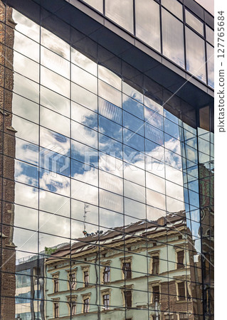 Modern Building Reflecting Old Architecture and Blue Sky in Glass Windows 127765684