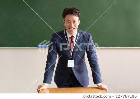 A male teacher standing in front of a blackboard and talking 127767190
