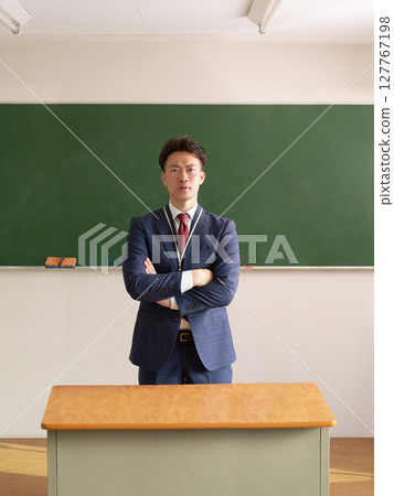 A male teacher standing in front of a blackboard with his arms folded A male teacher standing in front of a blackboard with his arms folded 127767198