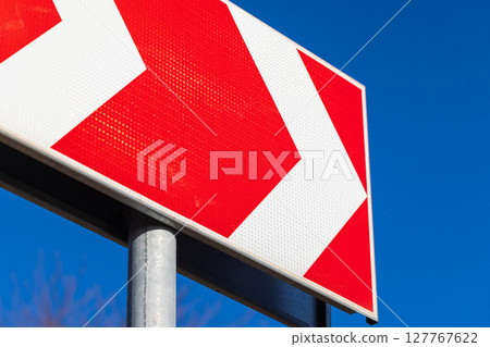A red directional road sign with white chevrons pointing to the right A red directional road sign with white chevrons pointing to the right 127767622