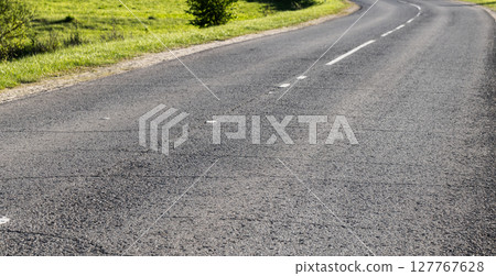 An empty curved asphalt road stretches through a lush green countryside An empty curved asphalt road stretches through a lush green countryside 127767628