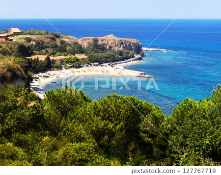Panoramic distant view of a beautiful blue beach in Calabria, Italy, where the vibrant shades of the Tyrrhenian Sea meet the pristine coastline. From afar, the beach stretches like a peaceful ribbon Panoramic distant view of a beautiful blue beach in Calabria, Italy, where the vibrant shades of the Tyrrhenian Sea meet the pristine coastline. From afar, the beach stretches like a peaceful ribbon 127767719