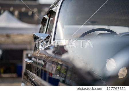 The side mirror of the classic car shines brightly, reflecting its vintage charm and polished craftsmanship. Though old, it maintains a fresh appearance with a simple design and glossy surface. 127767851