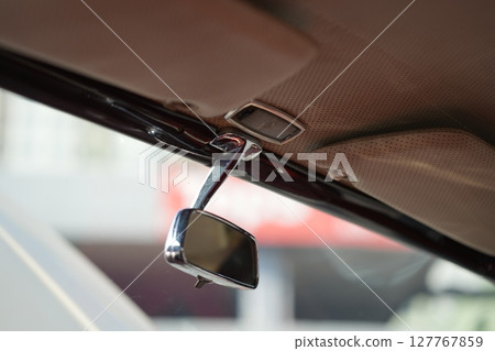 The rearview mirror of a classic car has a shiny chrome finish with a simple design, serving as a practical feature that adds elegance to the interior. 127767859