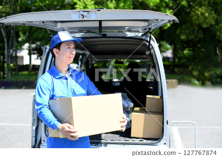 Asian male delivery man carrying packages in front of a mini van 127767874