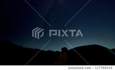 Silhouette of a man leaning against a car and looking up at the stars 127768419