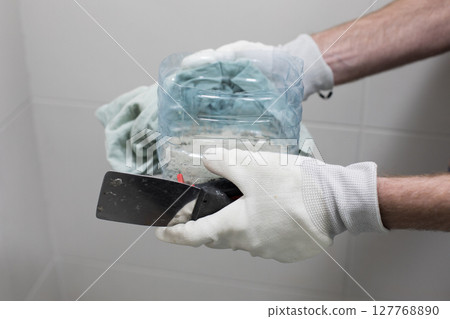 Trowel and cement glue for bathroom renovation work in male hands close up 127768890