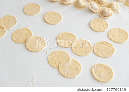 Raw homemade dumpling dough circles and raw dumplings on a white surface. Raw homemade dumpling dough circles and raw dumplings on a white surface. 127769119