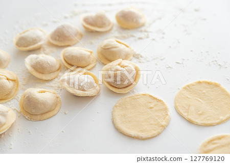 Raw homemade dumpling dough circles and raw dumplings on a white surface. 127769120