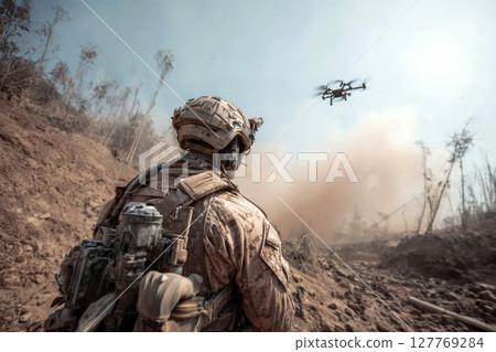 Soldier Observing Drone in a Post-Battlefield Desert Landscape. 127769284