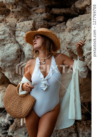 Woman Beachwear Summer Fashion Posing - A woman in a white swimsuit and a straw hat is standing in front of a rock wall. 127769708