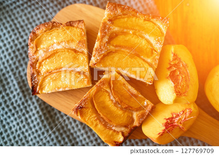 A dessert made of sliced peaches is on a wooden cutting board. The dessert is covered in sugar and looks delicious. A dessert made of sliced peaches is on a wooden cutting board. The dessert is covered in sugar and looks delicious. 127769709