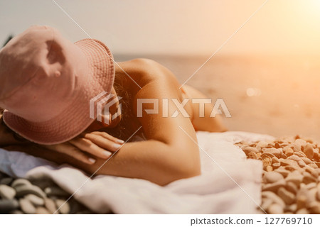 A woman sunbathes on the beach, lying on her stomach in a red swimsuit against the sea backdrop. 127769710