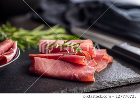 Sliced beef pastrami on cutting board on black table. 127770723
