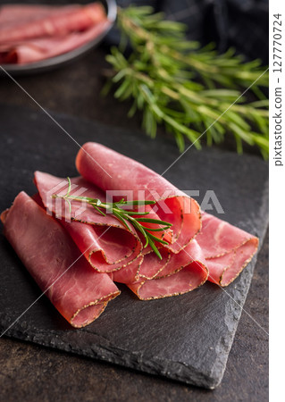 Sliced beef pastrami on cutting board on black table. 127770724