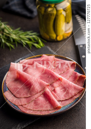 Sliced beef pastrami on plate on black table. Sliced beef pastrami on plate on black table. 127770725