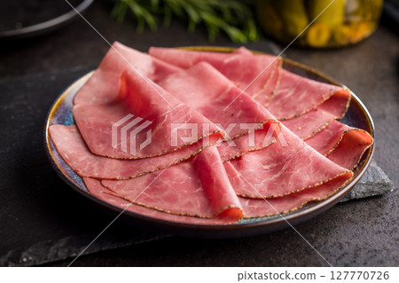 Sliced beef pastrami on plate on black table. Sliced beef pastrami on plate on black table. 127770726