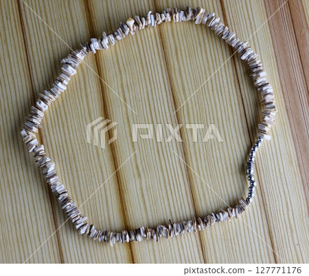 Handmade polished beige shell pieces necklace as a gift for a woman on a wooden background. Natural jewelry. Summer jewelry. 127771176