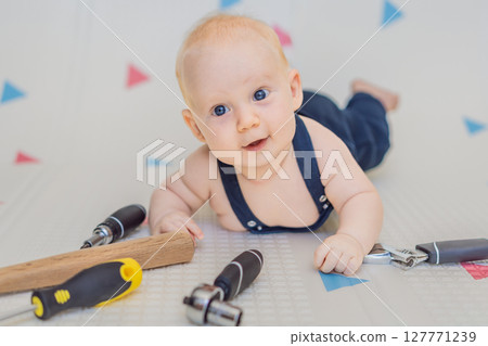 Adorable baby in a mechanic costume surrounded by toy tools. Concept of repair, imaginative play, and introducing kids to the world of fixing and problem-solving through fun Adorable baby in a mechanic costume surrounded by toy tools. Concept of repair, imaginative play, and introducing kids to the world of fixing and problem-solving through fun 127771239
