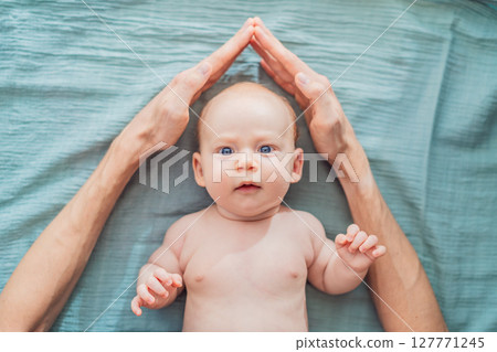 Father hands form a protective roof above baby head. Concept of safety, love, family protection, and emotional security in early childhood Father hands form a protective roof above baby head. Concept of safety, love, family protection, and emotional security in early childhood 127771245