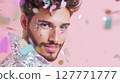 Portrait of young man with glitter makeup and sequin outfit looking at camera with confetti falling on pink background. Studio shot with soft lighting. LGBT pride, queer identity, and self-expression 127771777