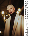 Fashionable young man with platinum blonde hair wearing elegant coat posing in warm ambient lighting. Studio portrait with bokeh lights. Modern style, gender expression, and fashion identity concept 127771790