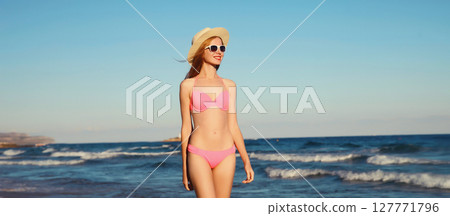 Summer vacation, beautiful happy slim woman in pink bikini swimsuit, tourist hat on the beach on sea 127771796