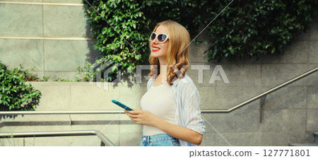 Stylish modern happy smiling young woman with phone in city park, girl holding smartphone on street Stylish modern happy smiling young woman with phone in city park, girl holding smartphone on street 127771801