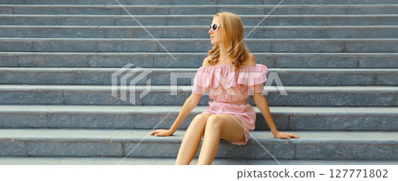 Beautiful modern young woman sitting on the stairs on city street in summer dress Beautiful modern young woman sitting on the stairs on city street in summer dress 127771802