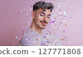 Young man with silver hair and glitter outfit smiling with closed eyes under falling confetti on pink background. Studio portrait with soft lighting. LGBT pride, queer identity, and self-expression 127771808