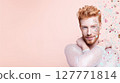 Confident young man with glitter makeup and sequin outfit posing on pastel pink background with falling confetti. Studio portrait with soft lighting. LGBT pride, queer identity, and celebration 127771814