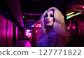 Drag queen with glamorous makeup and long blonde wig posing in neon-lit hallway of night club. Studio portrait with colorful lighting. Drag performance and LGBT concept. Design for poster, banner 127771822