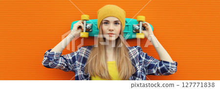 Portrait of stylish young girl with skateboard in hat, modern teenage female posing on orange Portrait of stylish young girl with skateboard in hat, modern teenage female posing on orange 127771838
