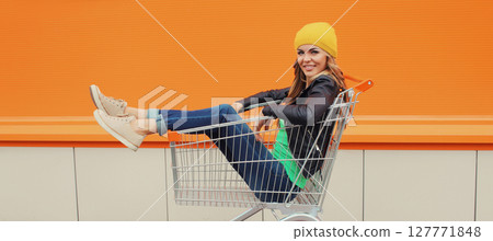 Beautiful happy smiling young blonde woman having fun sitting in shopping trolley cart in the city 127771848