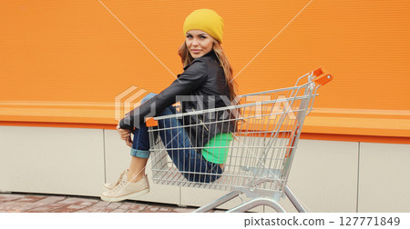 Beautiful happy smiling young blonde woman having fun sitting in shopping trolley cart in the city 127771849