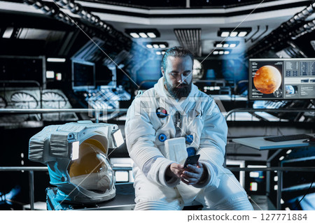 Lonely astronaut using smartphone to text friends before landing spaceship on Mars. Isolated man using phone to chat with family during mission to red planet surface in deep space Lonely astronaut using smartphone to text friends before landing spaceship on Mars. Isolated man using phone to chat with family during mission to red planet surface in deep space 127771884