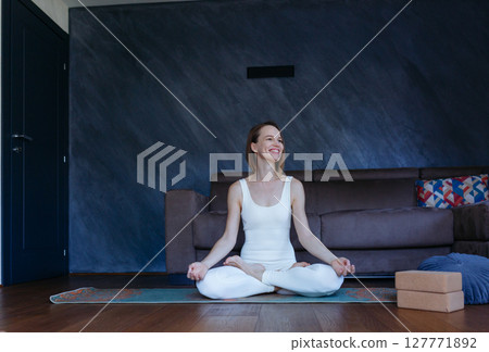 smiling woman sitting in lotus yoga pose doing exercise at home smiling woman sitting in lotus yoga pose doing exercise at home 127771892