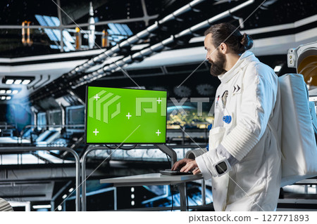 Astronaut in starship using green screen monitor to confirm suit integrity. Orbital station crew member testing gear during routine equipment check using chroma key mockup display 127771893