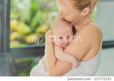 Mother gently hugging her baby at home, sharing a warm and loving moment. Parenthood, family bonding, and maternal love concept 127772103